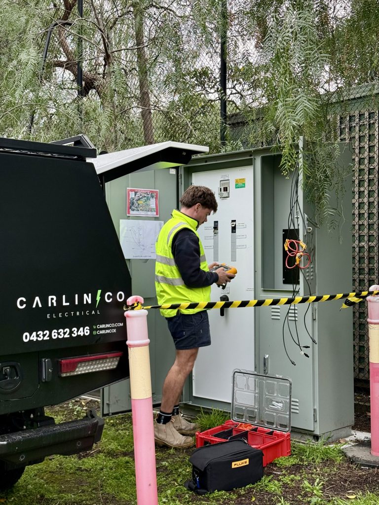 Carlin Co electrician installing power logging equipment at a commercial switchboard