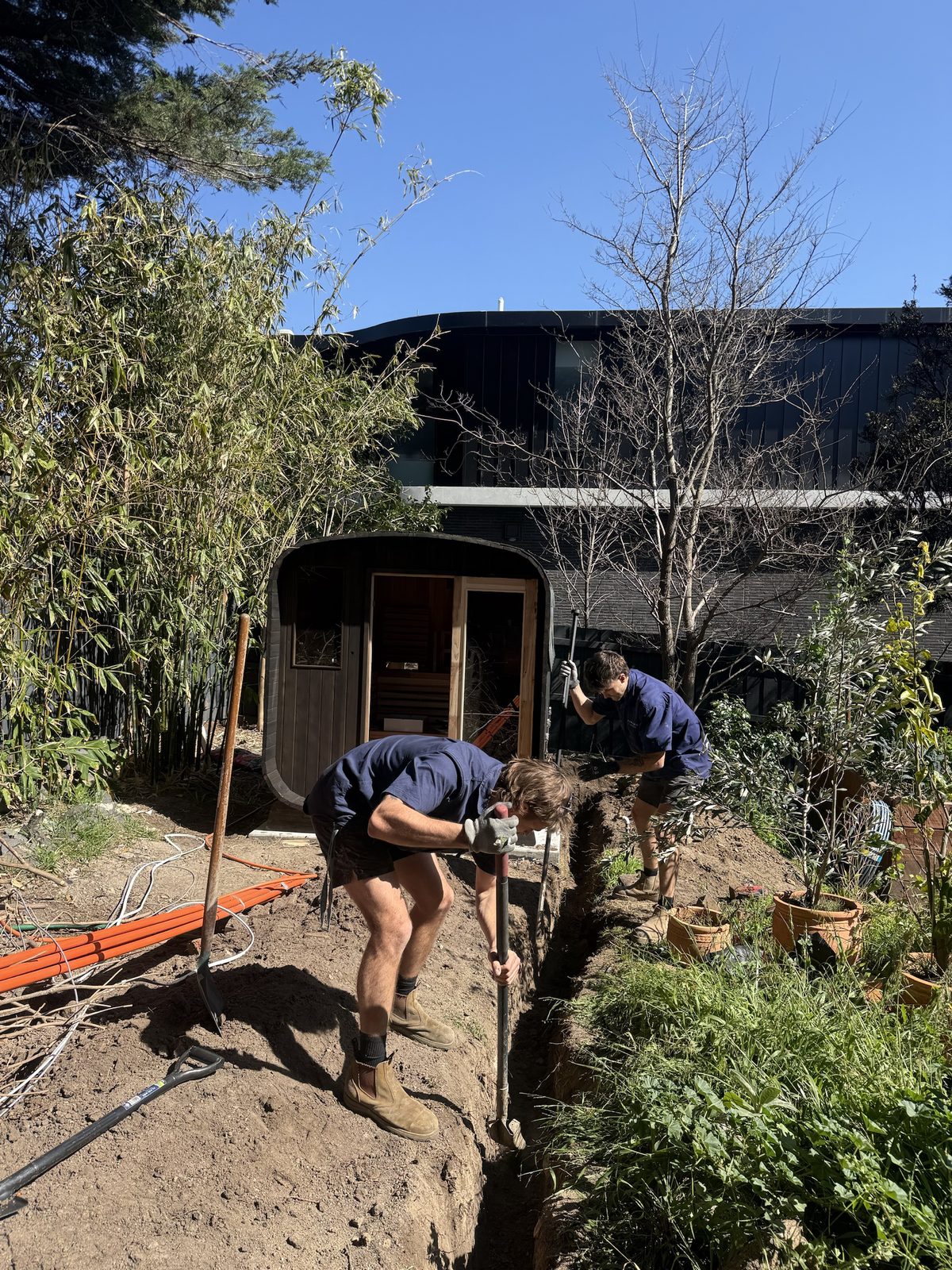 Carlin Co electricians hand-trenching underground conduit run for cabin sauna power supply in Kew